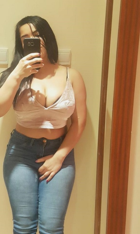 A young woman in casual attire posing for a selfie with a cheerful expression.